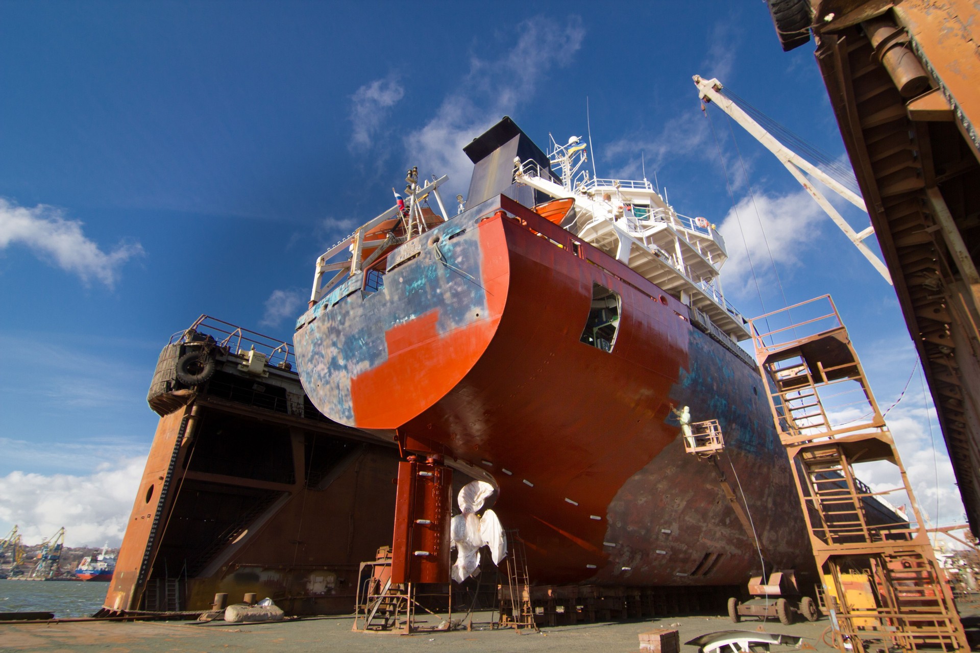Commercial vessel in dry dock for maintenance. Ship undergoes hull painting and repairs. Maritime, industrial shipping process. Workers refurbish boat. Dockyard activity, sea transport upgrade.